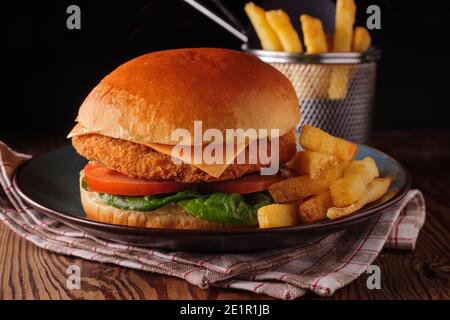 Filet de poulet dans un pain de brioche avec laitue tomates, fromage et peau sur des frites tournées avec créativité éclairage Banque D'Images