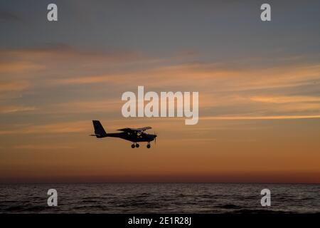 Silhouette minuscule d'avion de 2 places survolant la mer Baltique pendant coucher de soleil coloré Banque D'Images