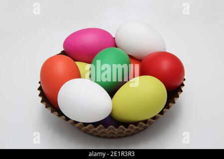 Œufs de pâques peints en plusieurs couleurs en rouge, rose, jaune, vert et blanc dans un panier en papier brun sur fond blanc. Banque D'Images