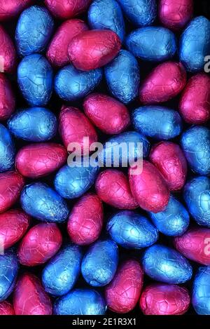 Pile ou groupe de plusieurs couleurs et différentes tailles d'oeufs de pâques au chocolat enveloppés de papier d'aluminium coloré en bleu et rose. Banque D'Images