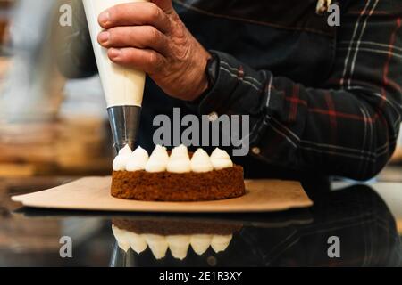 Gros plan sur les mains d'un chef pâtissier remplissant un gâteau à la crème avec un sac à passepoil Banque D'Images