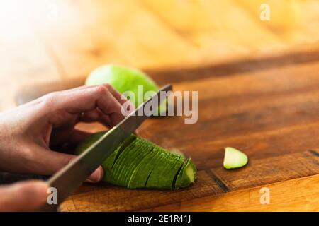 Gros plan des mains coupant de l'avocat avec un couteau sur un planche en bois Banque D'Images