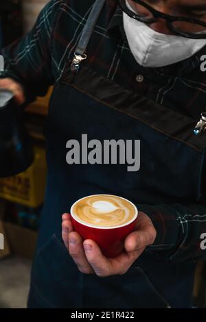 Gros plan d'un barista masqué méconnaissable qui prépare un cappuccino une tasse rouge Banque D'Images