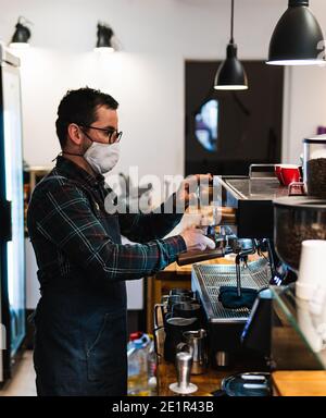 Barista caucasien avec masque pour faire du café dans un café Banque D'Images