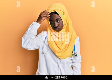 Belle jeune femme africaine portant un uniforme de médecin et hijab inquiet et stressé au sujet d'un problème de main sur le front, nerveux et anxieux pour l'irc Banque D'Images