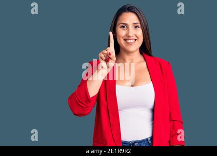 Jeune belle brune femme portant des vêtements élégants montrant et pointant vers le haut avec le doigt numéro un tout en souriant confiant et heureux. Banque D'Images