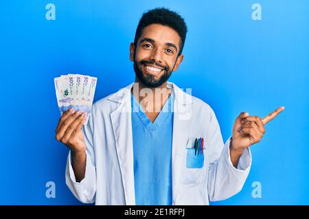 Beau hispanique homme avec barbe portant l'uniforme de médecin tenue 50 les pesos colombiens souriant se contenent de pointer du doigt et de la main vers le côté Banque D'Images