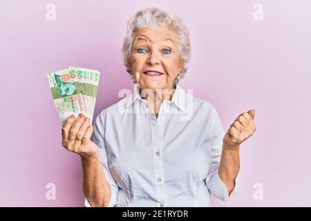 La sénior à cheveux gris, qui détient des billets de 50 dollars de hong kong, crie fièrement, célébrant la victoire et le succès très excités par le bras relevé Banque D'Images