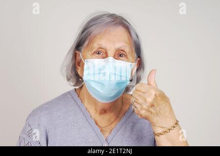 Bonne femme masquée senior avec le pouce vers le haut après avoir reçu COVID vaccin Banque D'Images