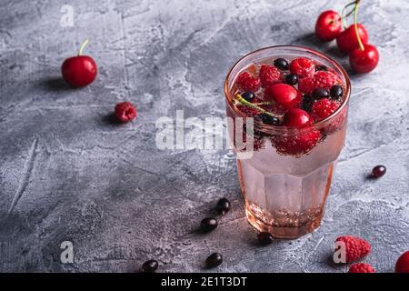 Eau fraîche et gazeuse buvez de cerise, framboise et baies de cassis en verre à facettes rouge sur fond de béton de pierre, boisson diététique d'été, un Banque D'Images