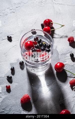 Eau fraîche et gazeuse boire avec baies de cerise, framboise et cassis en verre transparent sur fond de béton de pierre, boisson diététique d'été, a Banque D'Images