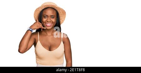 Jeune femme noire portant un chapeau d'été souriant faisant un geste de téléphone avec la main et les doigts comme parler au téléphone. Communiquer des concepts. Banque D'Images