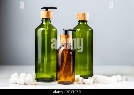 Ensemble de flacons cosmétiques en verre vert et marron avec pompes et éléments en bois pour le réapprovisionnement des produits de beauté. Accessoires de salle de bain minimalistes Banque D'Images