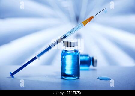 Seringue et flacons de liquide bleu représentant le traitement du vaccin sur une surface médicale stérile dans un environnement conceptuel Banque D'Images