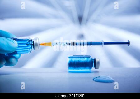Seringue et flacons de liquide bleu représentant le traitement du vaccin sur une surface médicale stérile dans un environnement conceptuel Banque D'Images