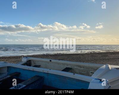 Pett Level Beach au coucher du soleil. Piscine d'eau de mer et rochers en premier plan. Winchelsea Beach rencontre les falaises une forêt pétrifiée visible à marée basse Banque D'Images