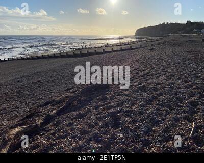 Pett Level Beach au coucher du soleil. Piscine d'eau de mer et rochers en premier plan. Winchelsea Beach rencontre les falaises une forêt pétrifiée visible à marée basse Banque D'Images