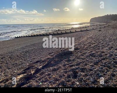 Pett Level Beach au coucher du soleil. Piscine d'eau de mer et rochers en premier plan. Winchelsea Beach rencontre les falaises une forêt pétrifiée visible à marée basse Banque D'Images