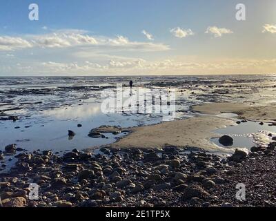 Pett Level Beach au coucher du soleil. Piscine d'eau de mer et rochers en premier plan. Winchelsea Beach rencontre les falaises une forêt pétrifiée visible à marée basse Banque D'Images