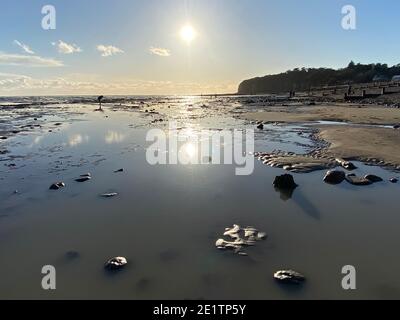 Pett Level Beach au coucher du soleil. Piscine d'eau de mer et rochers en premier plan. Winchelsea Beach rencontre les falaises une forêt pétrifiée visible à marée basse Banque D'Images