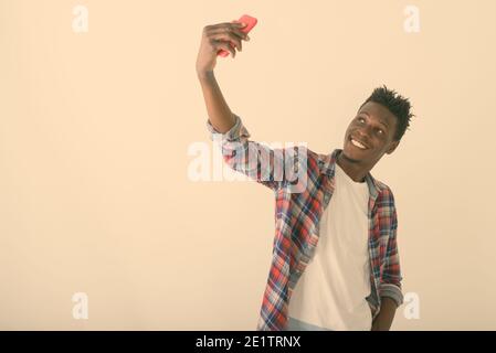 Studio shot of young happy black African man smiling tout en tenant avec photo selfies téléphone mobile contre fond blanc Banque D'Images