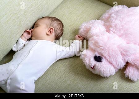 Bébé dort dans la chambre, bébé rêve sur le canapé à la maison. Vue de dessus de bébé endormi et jouet rose doux sur le canapé. Petit enfant dans la barboteuse allongé sur sa ba Banque D'Images