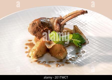 Côtelettes d'agneau rôties dans une jaquette de bacon avec pommes de terre, oignons et feuilles de menthe dans un plat blanc Banque D'Images