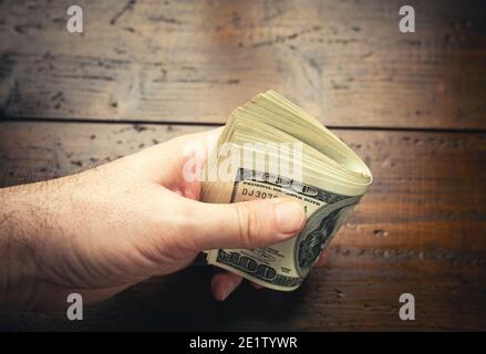 Main tenant cent billets américains sur fond de table en bois. Espèces de billets de cent dollars, monnaie papier. Banque D'Images