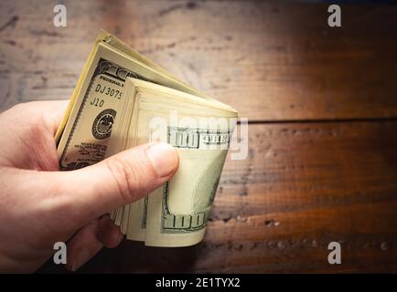 Main tenant cent billets américains sur fond de table en bois. Espèces de billets de cent dollars, monnaie papier. Banque D'Images