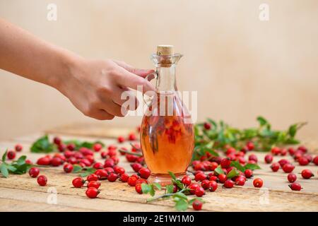 À la main, déposer une fiole avec de l'huile de rosehip rose une table marron Banque D'Images