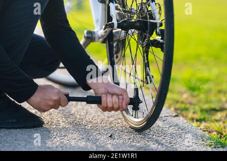 Homme pompant la roue de vélo dans le parc. L'homme gonfle la roue du vélo à l'aide d'une pompe. Pomper de l'air dans une roue de vélo vide. Banque D'Images