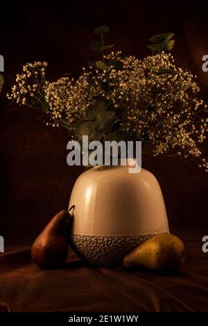 Vase blanc doux avec fleurs « Baby's Breath » sur fond sombre, les fruits artificiels ajoutent une touche agréable. Banque D'Images