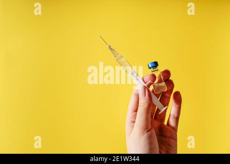 Gros plan sur la main de la femme caucasienne inconnue médecin tenant seringue avec aiguille et injection de vaccin devant le jaune mur - covid-19 coronavirus va Banque D'Images
