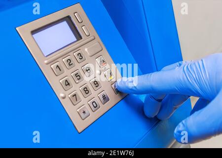 La main d'un homme dans des gants médicaux de protection compose un code PIN au terminal pour émettre de l'argent, gros plan. Banque D'Images