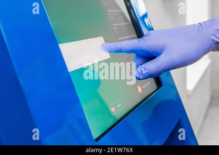 La main d'un homme dans un gant médical de protection appuie sur l'écran tactile du terminal pour émettre des billets électroniques, gros plan. Banque D'Images