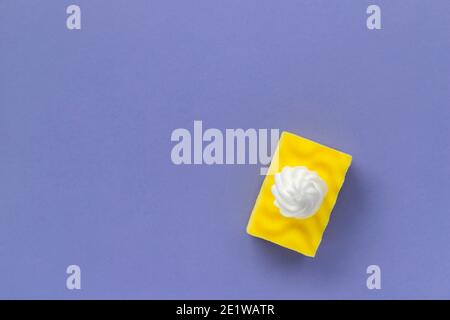 Éponge jaune pour laver la vaisselle avec mousse sur fond violet Banque D'Images