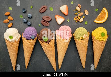 Divers de saveur de crème glacée en cônes bleuet, pistache, amande, orange et chocolat sur fond de pierre sombre. Concept de menu été et sucré Banque D'Images