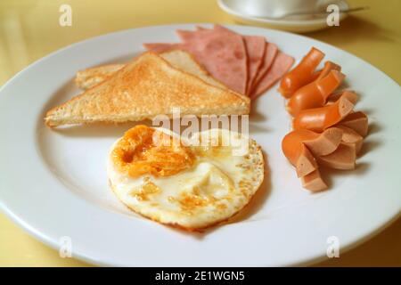 Assiette d'œufs frits en forme de coeur, saucisses et jambons avec toasts pour le petit déjeuner Banque D'Images