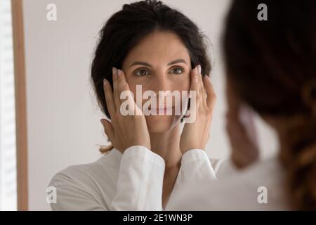 Jeune belle femme regarder dans le miroir massant visage Banque D'Images