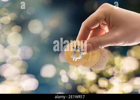 Une fille tient une pièce de monnaie Bitcoin dans la main contre le fond des chartes de commerce. Crypto-monnaie Banque D'Images