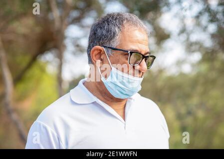 Portrait homme âgé seul voyageur porte un masque et voyage dans une forêt. Le vieil homme porte un masque facial, de la mauvaise façon, l'usure incorrecte - les masques devraient couvrir le nez. Banque D'Images