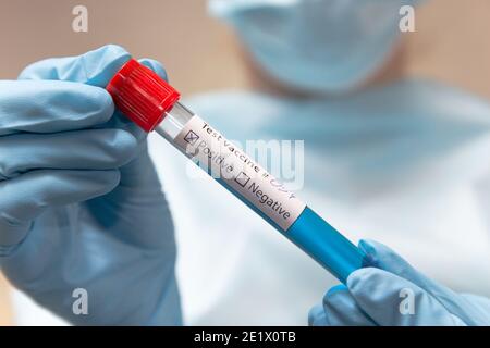 Vaccin contre le coronavirus, positif. Le médecin en costume de protection, masque médical et gants en latex tient un tube à essai avec un vaccin. Banque D'Images