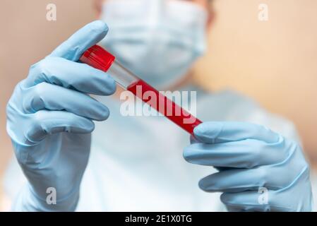 Test sanguin du coronavirus. Le médecin en costume de protection, masque médical et gants en latex tient un tube à essai avec du sang. Banque D'Images