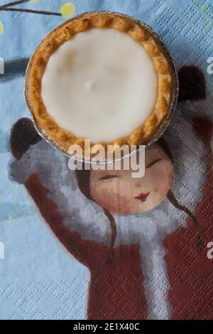 Tarte aux pommes de terre hachée glacée de Sainsburys sur une serviette de Noël festive - pâtisseries fourrées de viande hachée, recouvertes de glaçage blanc doux Banque D'Images