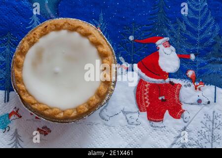 Tarte aux pommes de terre hachée glacée de Sainsburys sur une serviette de Noël festive - pâtisseries fourrées de viande hachée, recouvertes de glaçage blanc doux Banque D'Images