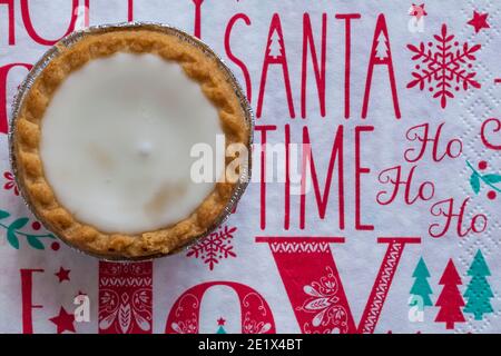 Tarte aux pommes de terre hachée glacée de Sainsburys sur une serviette de Noël festive - pâtisseries fourrées de viande hachée, recouvertes de glaçage blanc doux Banque D'Images