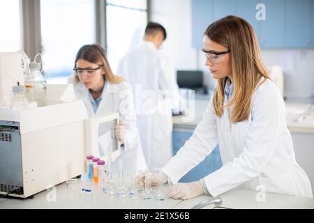 Jeunes femmes scientifiques dans un flacon de mise en blouse de laboratoire blanc avec un échantillon pour une analyse sur un système d'ionchromatographie en laboratoire biomédical Banque D'Images