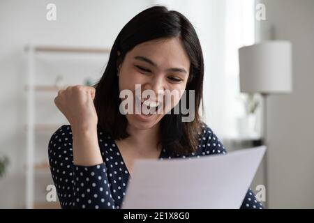 Une femme asiatique heureuse et émotive lisant la notification d'admission à l'université. Banque D'Images