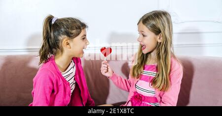 Gros plan de deux petites filles heureuses avec une boucle en forme de coeur debout ensemble à la maison. Concept d'amitié pour les enfants de la Saint-Valentin Banque D'Images