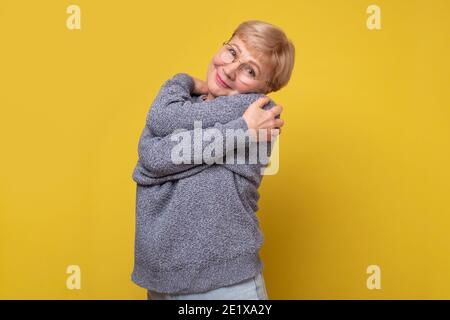 Portrait d'une heureuse dame âgée mûre et joyeuse qui s'embrasse. Studio tourné sur un mur jaune. Banque D'Images